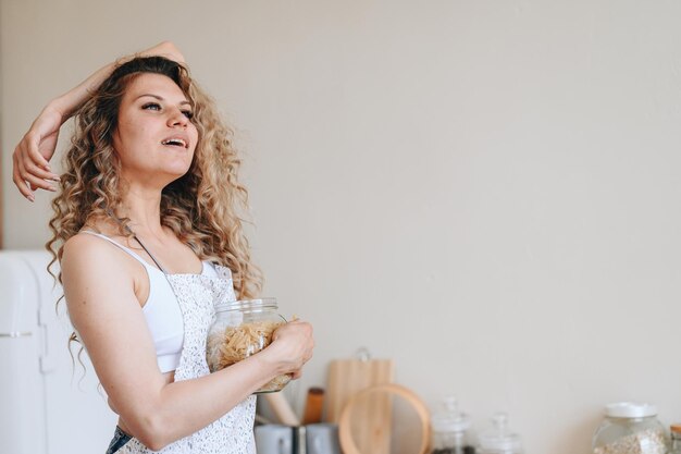 Donna riccia in un grembiule tiene un barattolo di pasta Donna che pensa a cosa cucinare per cena Spazio di copia