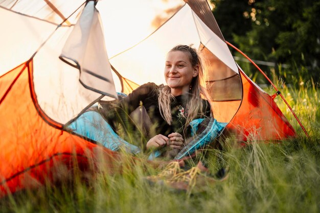 Donna rilassante e sdraiarsi in un sacco a pelo nella tenda Campeggio al tramonto nella foresta Montagne paesaggio viaggio stile di vita campeggio Viaggio estivo avventura all'aria aperta