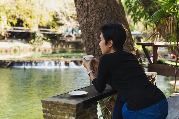 Donna rilassata che tiene il caffè della tazza che si siede sulla sedia vicino al fiume