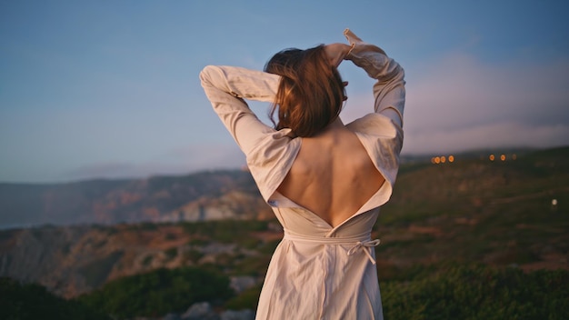 Donna romantica che balla al tramonto la natura fa movimenti rilassati sulla scogliera dell'oceano