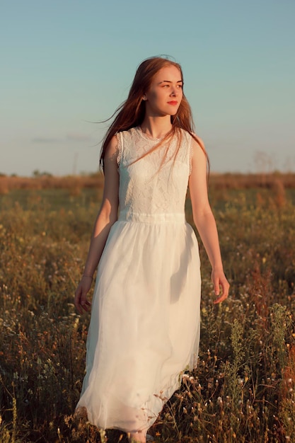 Donna romantica che balla in un meraviglioso campo di fiori colori caldi del tramonto vestito bianco colori morbidi