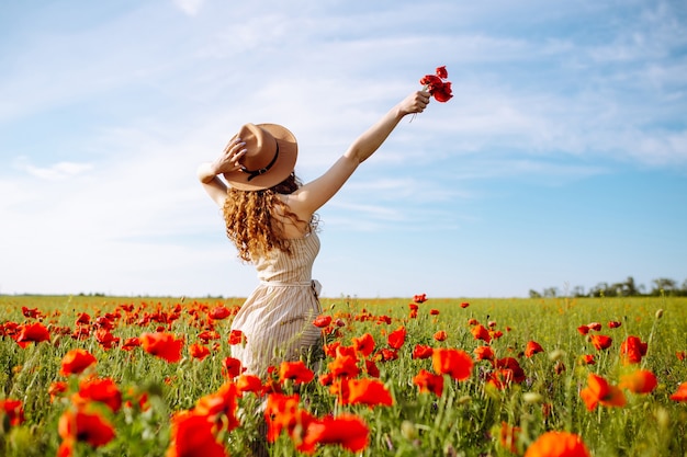 Donna romantica con fiore in mano che soggiorna in un campo di papaveri