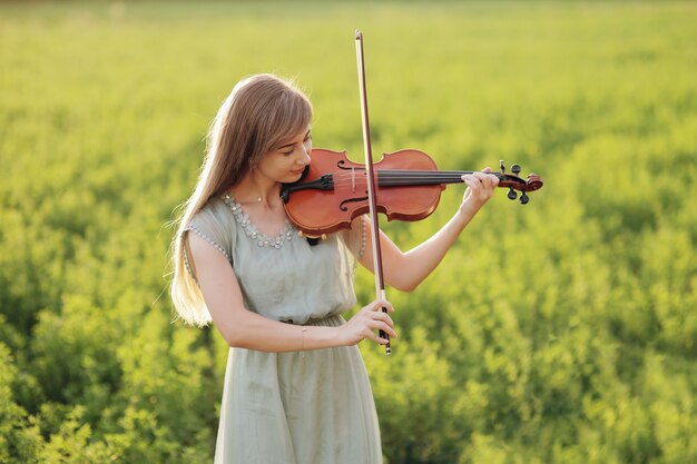 Donna romantica con i capelli sciolti a suonare il violino. Luce del tramonto in natura. Formazione al violino