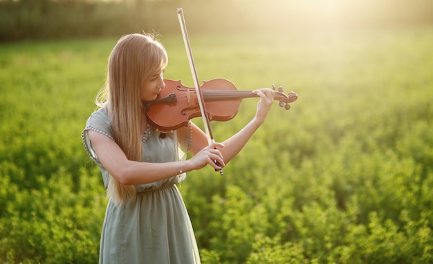 Donna romantica, ragazza con i capelli sciolti, suonare il violino. Luce del tramonto in natura