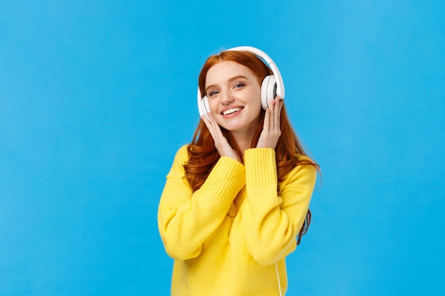 Donna rossa attraente e spensierata alla moda nella musica d'ascolto del maglione giallo con le cuffie