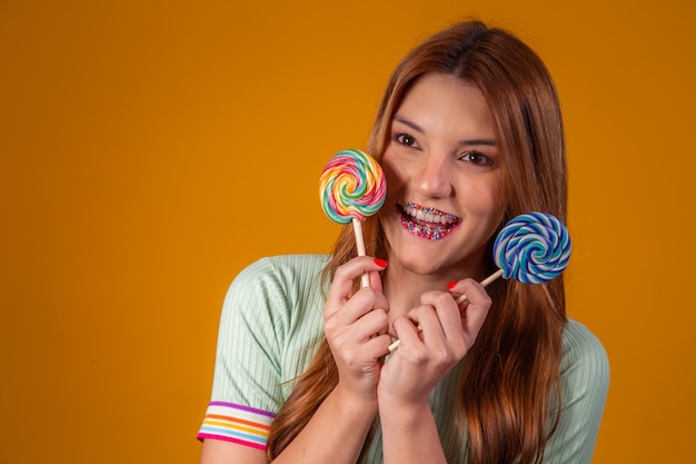 Donna rossa brasiliana con due lecca-lecca su sfondo giallo che sorride alla telecamera