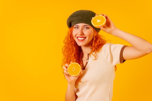 Donna rossa che tiene un'arancia su sfondo giallo isolato sorridente con un frutto