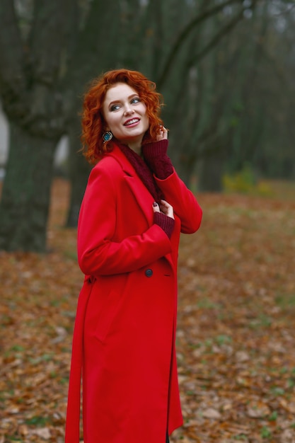 Donna rossa con i capelli in cappotto rosso su sfondo autunnale.