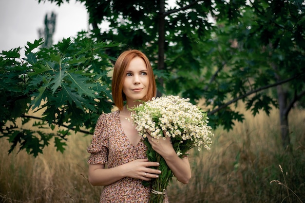 Donna rossa di quarant'anni con un grande mazzo di fiori di campo in estate nella natura