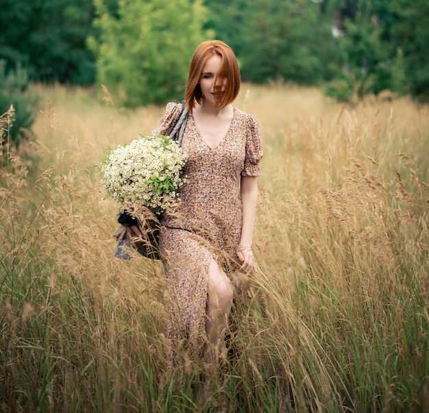Donna rossa di quarant'anni con un grande mazzo di fiori di campo in estate nella natura
