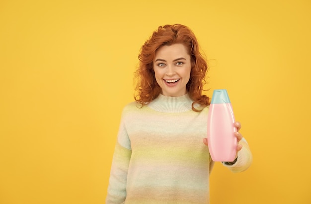 Donna rossa felice con capelli ricci che offre shampoo o balsamo per la cura del corpo