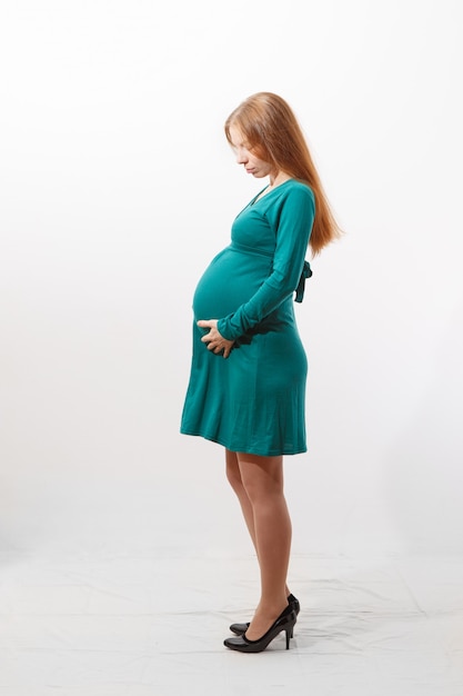 Donna rossa incinta con la sua grande pancia che indossa un vestito verde girato in uno studio bianco