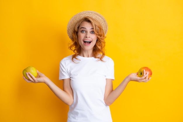 Donna rossa sorridente in cappello di paglia estivo con denti sani che tengono il ritratto isolato dello studio della mela