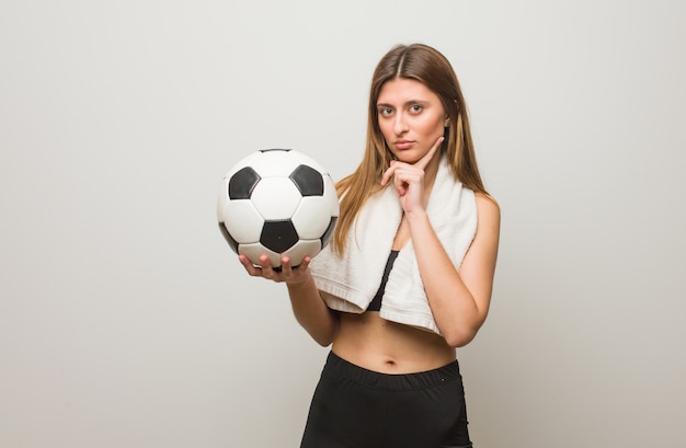 Donna russa di giovane forma fisica che dubita e confusa. In possesso di un pallone da calcio.