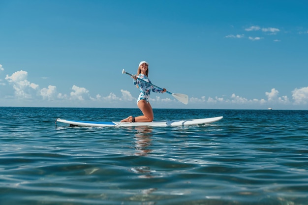 Donna sana e felice in forma in bikini che si rilassa su una tavola da surf sup che galleggia sul limpido mare turchese