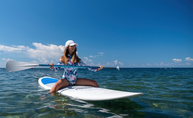 Donna sana e felice in forma in bikini che si rilassa su una tavola da surf sup che galleggia sul limpido mare turchese