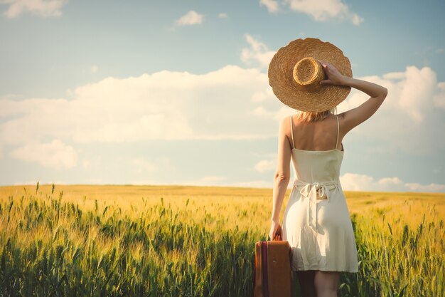 Donna sanguinante in cappello con la valigia nel campo di frumento nel tempo di tramonto