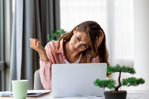 Donna scioccata esausta dal lavoro che studia sodo Annoiato e frustrato guardando il laptop Testa appoggiata a portata di mano Spazio luminoso grandi finestre Concetto di casa Concetto di stress