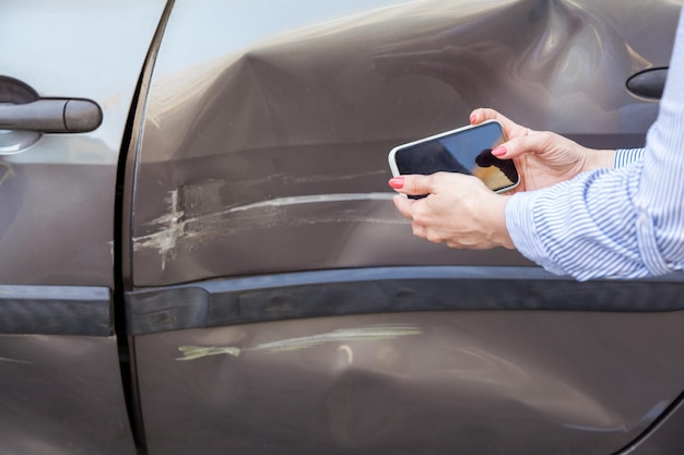 Donna sconosciuta con il cellulare in mano che fotografa la parte danneggiata dell'auto fotografando graffi e ammaccature sulla portiera dell'auto registra le conseguenze dell'incidente Scatto all'aperto