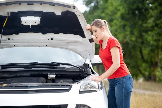 Donna sconvolta che guarda sotto il cofano dell'auto surriscaldata nel campo