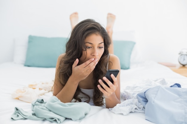 Donna scossa che esamina il telefono cellulare a letto