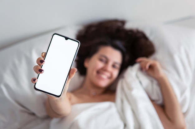 Donna sdraiata a letto che mostra il telefono con schermo bianco