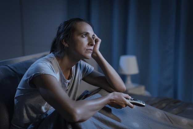 Donna sdraiata a letto di notte e guardando la televisione soffre di insonnia