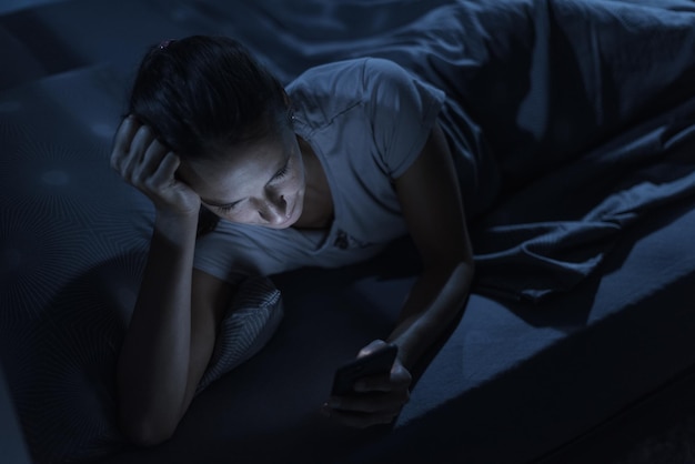 Donna sdraiata a letto di notte e in connessione con il suo telefono