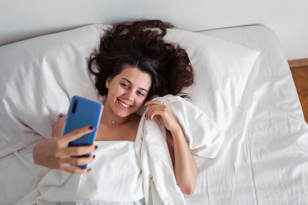 Donna sdraiata a letto prendendo selfie al telefono