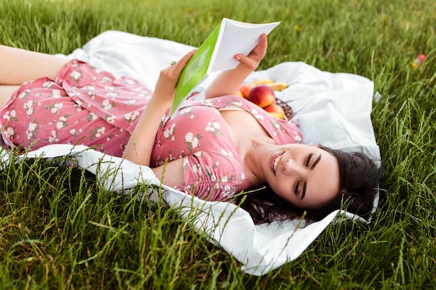 Donna sdraiata sul lenzuolo bianco, libro di lettura, sorridente