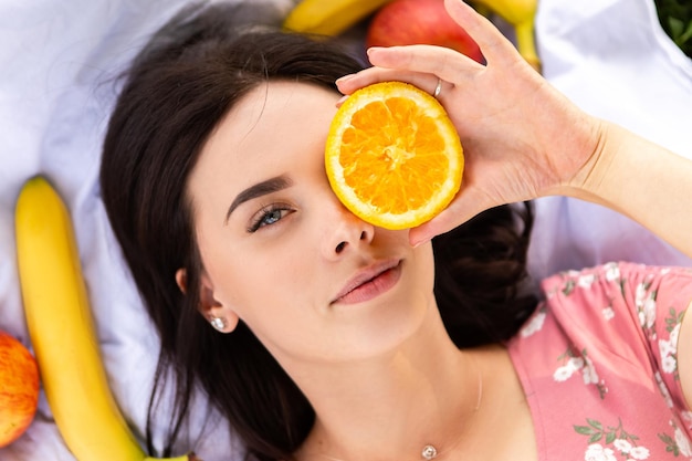 Donna sdraiata sul lenzuolo bianco sorridente e tenere una fetta d'arancia Signora riposarsi nel parco della città