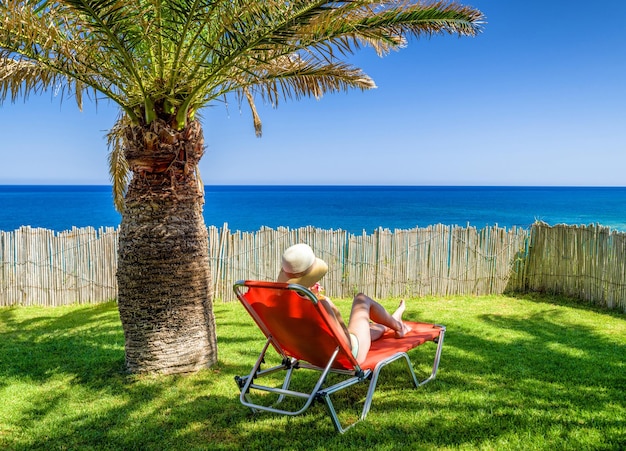 Donna sdraiata sul lettino in resort tropicale sotto le palme e bere bevande