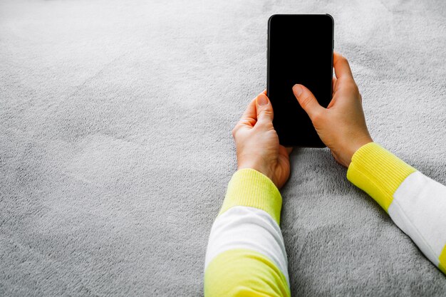 Donna sdraiata sul letto e tenendo in mano lo smartphone.