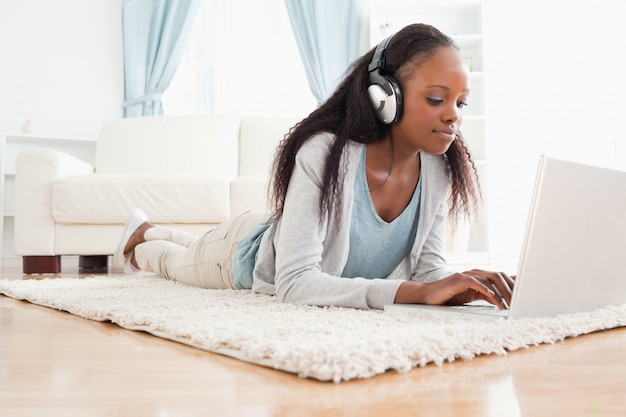 Donna sdraiata sul pavimento con il suo laptop ascoltando musica