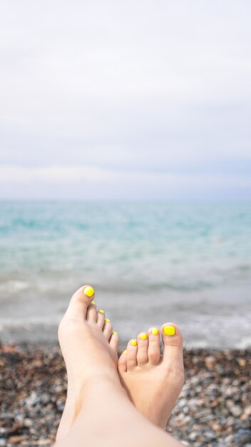 Donna sdraiata vicino all'acqua. Gambe di donna vicino al mare blu - foto verticale