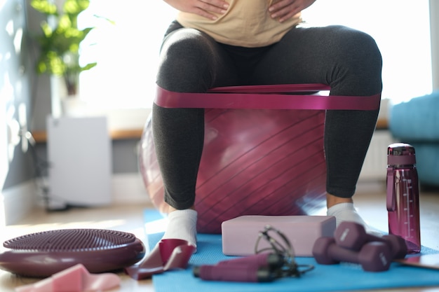 Donna seduta a casa su una palla sportiva, primo piano delle gambe. Sport durante una pandemia, supporto sanitario. Motivazione, forza