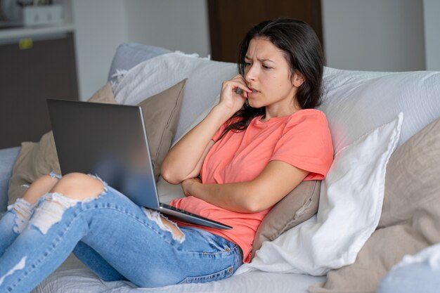 Donna seduta a casa sul divano con un laptop La ragazza ha problemi, è molto confusa. Molto lavoro