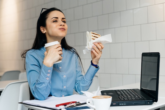 Donna seduta a tavola a bere caffè e mangiare panino