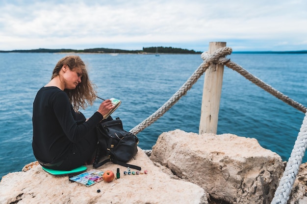 Donna seduta al bordo che disegna un'immagine di vista sul mare