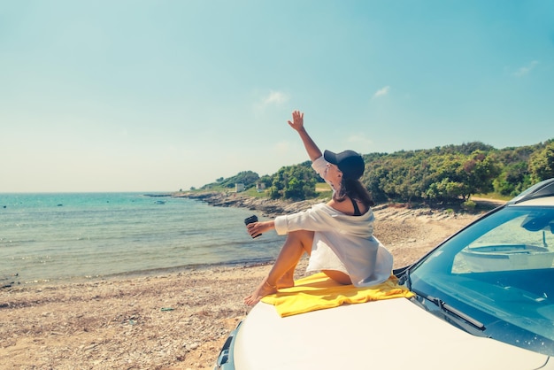 Donna seduta al cofano dell'auto che beve caffè godendo della vista sul mare