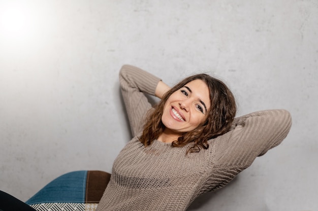 Donna seduta comodamente su una poltrona. Sorridente guardando la telecamera con le braccia dietro la testa.