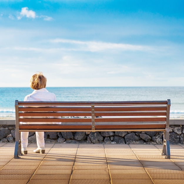 Donna seduta da sola su una panchina, guardando il mare