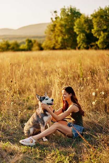 Donna seduta in campo con il cane bassotto sorridente mentre si trascorre del tempo in natura con il cane amico in autunno al tramonto durante il viaggio