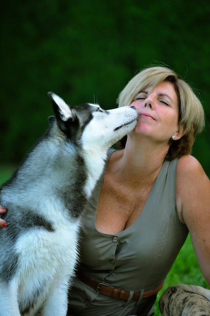 Donna seduta in giardino accanto a un husky siberiano bianco e nero che le lecca il viso