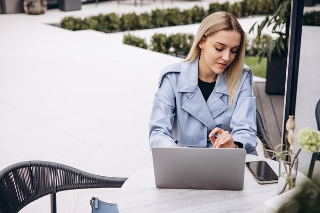 Donna seduta nella caffetteria che lavora al computer portatile e che beve caffè