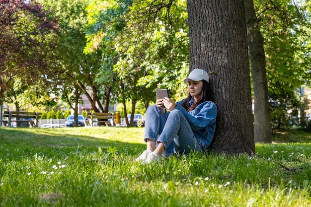 Donna seduta sotto l'albero che legge il libro elettronico