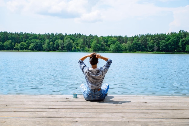 Donna seduta su un molo di legno che guarda il lago in una giornata di sole