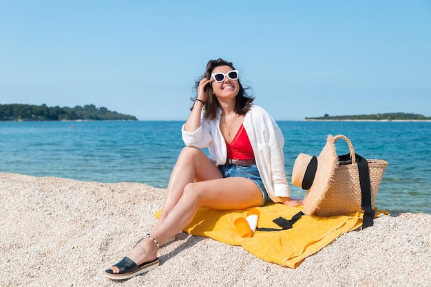 Donna seduta su una coperta gialla in mare spiaggia in abito estivo protezione della pelle del sole in bottiglie