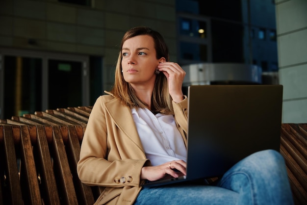 Donna seduta su una panchina all'aperto e che utilizza il concetto di laptop di lavoro a distanza e istruzione online