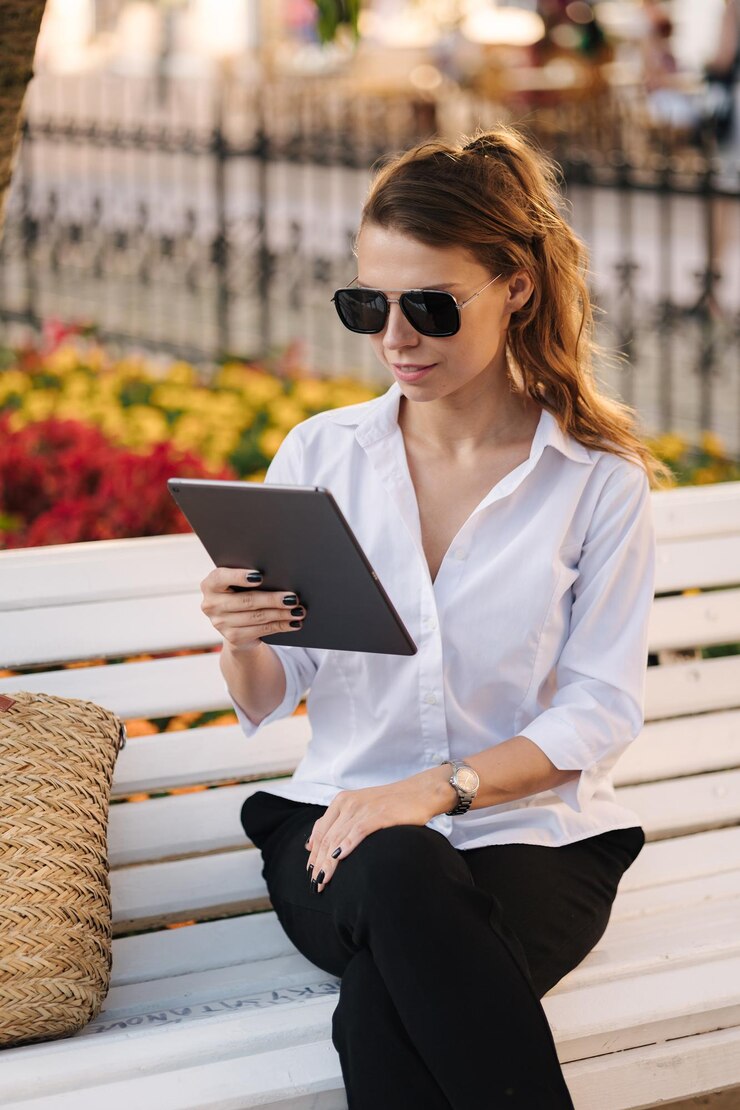 Donna seduta su una panchina nel parco e che lavora utilizzando il tablet libero professionista femminile